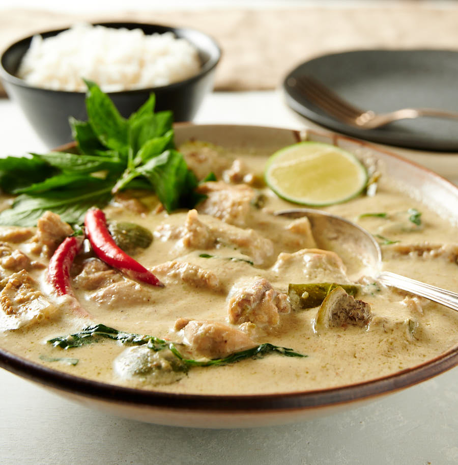 Bowl of Thai green curry from the front. Bowl of rice in the background.