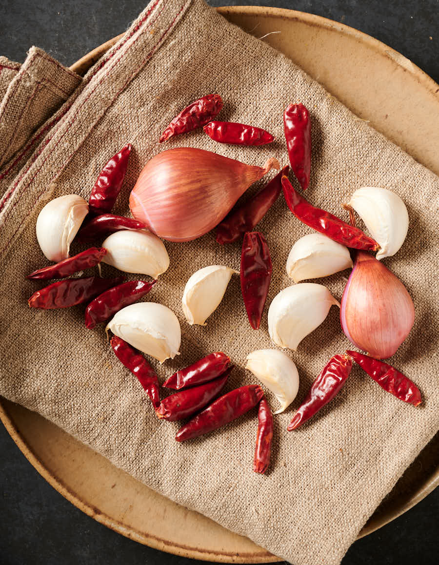 Garlic, chilies and shallots on a tan dishtowel from above.