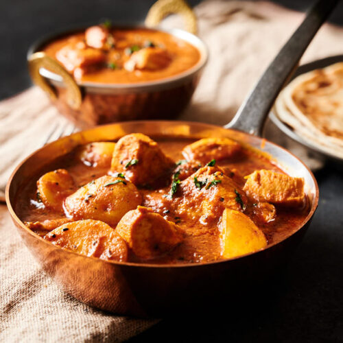 Moody scene of bengali chicken curry in a copper skillet from the front.