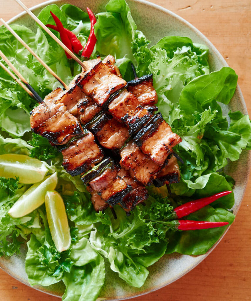 Grilled pork belly on a bed of lettuce with red chilies and lime wedges