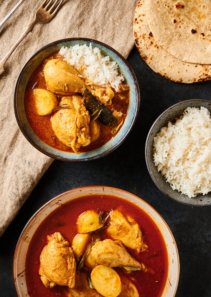 Table scene with kari ayam in a bowl with rice next to a serving platter filled with curry.