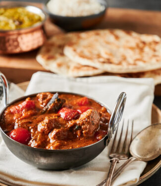 Lamb rogan josh in a black bowl with parathas from the front.