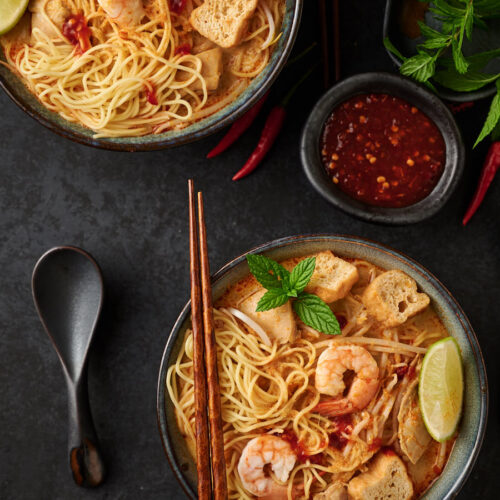 Curry laksa bowl with chopsticks and sambar from above.