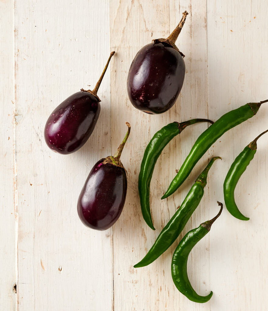 Indian eggplant and green chilies stewn on a white background.