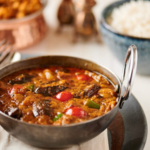 Eggplant curry in an iron bowl with rice and chana masala from the front.