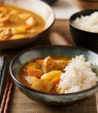 Bowl of Japanese chicken curry with rice with big bowl of curry in the background.