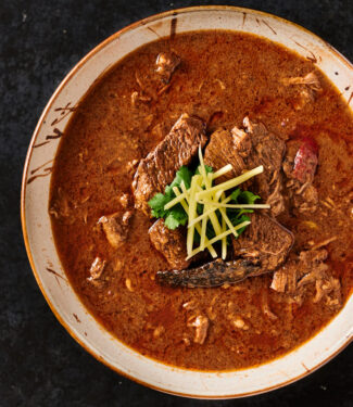 Serving bowl of nihari masala garnished with ginger and cilantro.