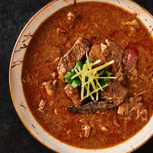 Serving bowl of nihari masala garnished with ginger and cilantro.