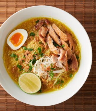 Bowl of soto ayam on bamboo background from above.