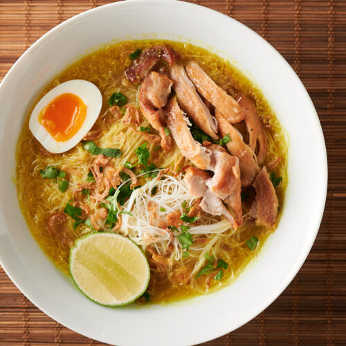 Bowl of soto ayam on bamboo background from above.