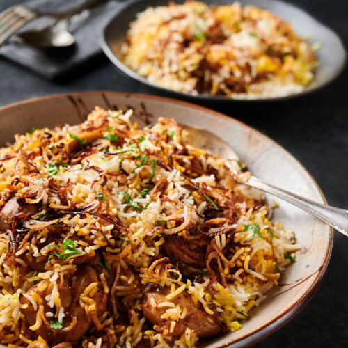 Chicken biryani in a bowl with serving spoon from the front.