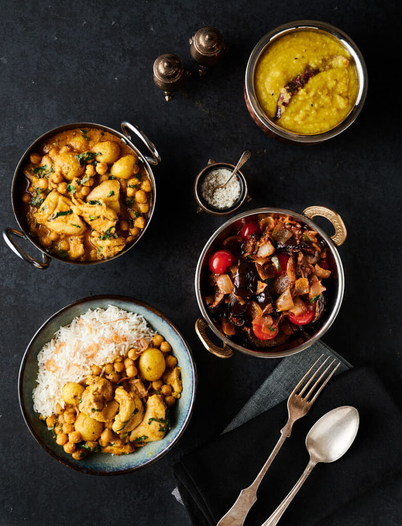 Table scene - chicken and chickpea curry, eggplant curry and dal from above.