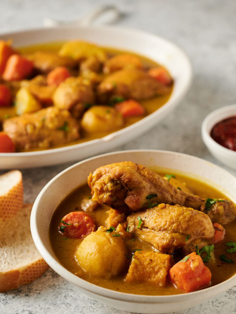 Bowl of chicken curry with serving dish in the background.