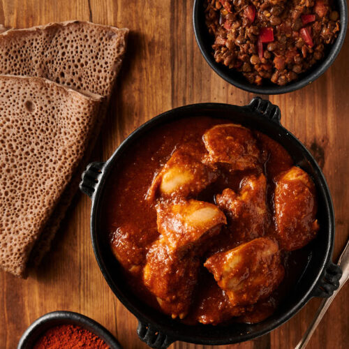 Door wat in a clay bowl with injera bread and lentils from above.