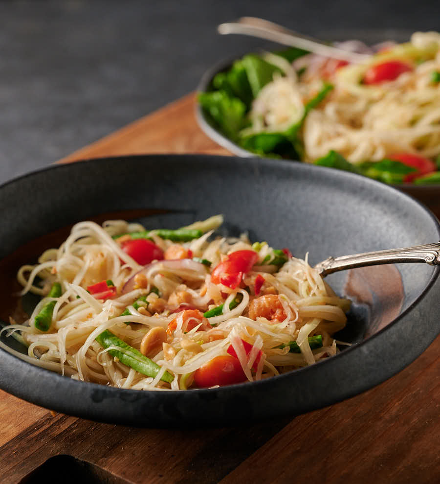 Serving of som tam - papaya salad in a clay bowl from the front.