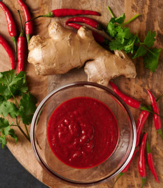 Tandoori paste in a clear bowl surrounded by ginger root and red chilies.