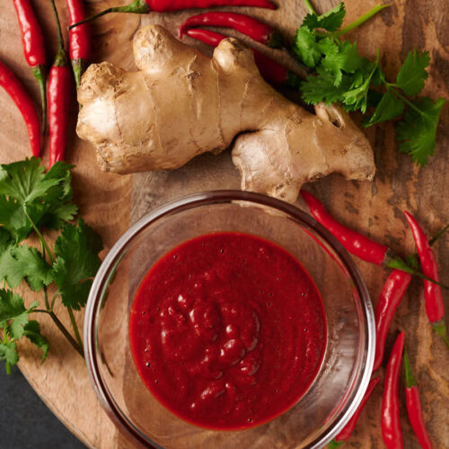 Tandoori paste in a clear bowl surrounded by ginger root and red chilies.