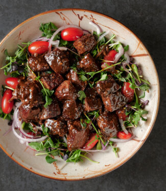 Bowl of shaking beef on a bed of micro-greens from above.