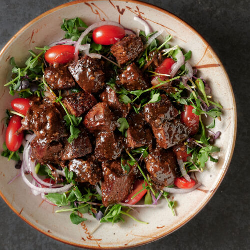 Bowl of shaking beef on a bed of micro-greens from above.