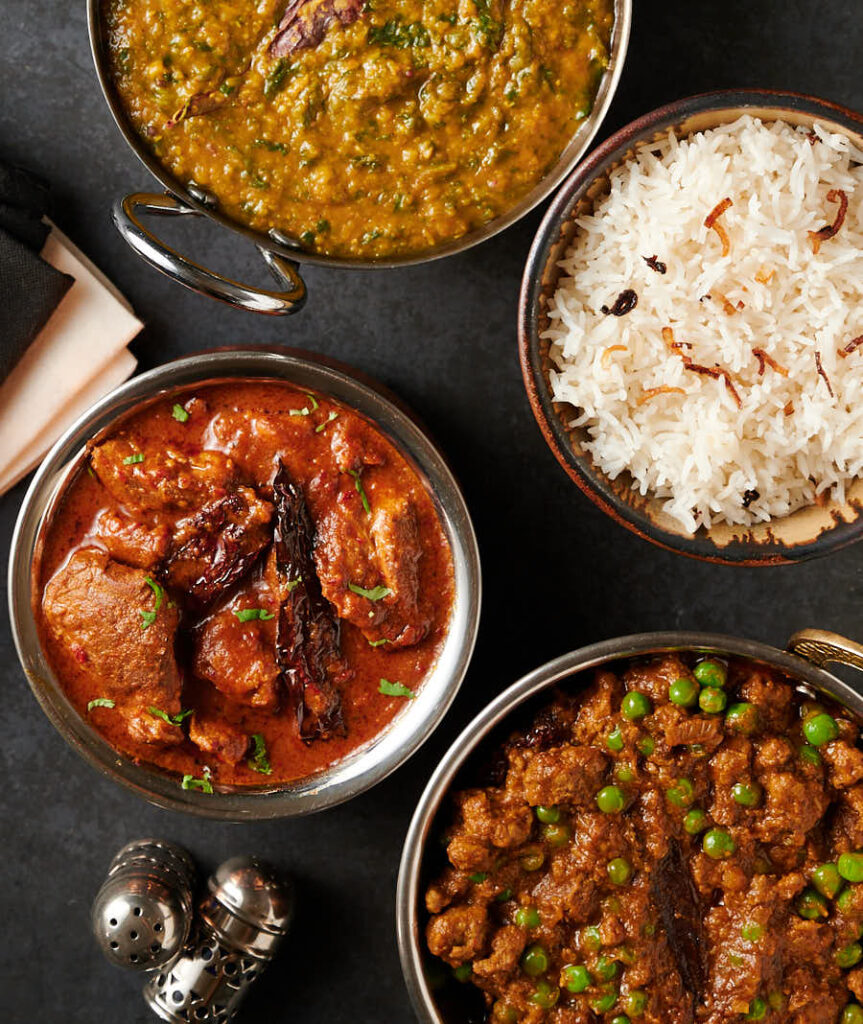 Lamb vindaloo, keema matar, dal palak and rice table scene from above.