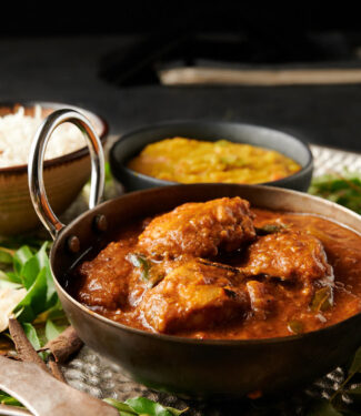 Chettinad chicken curry in a carbon steel bowl from the front. Dal and rice in the background.