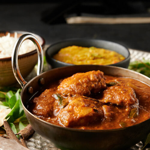 Chettinad chicken curry in a carbon steel bowl from the front. Dal and rice in the background.