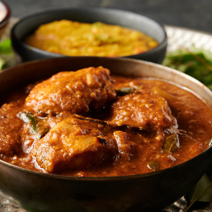 Closeup of chettinad chicken curry in a carbon steel bowl from the front.