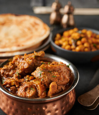 Lamb madras in a copper bowl with chana masala and parathas in the back ground.