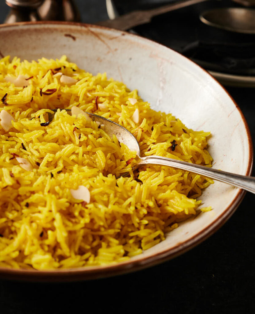 Bowl of indian restaurant style rice pilau with spoon from the front.