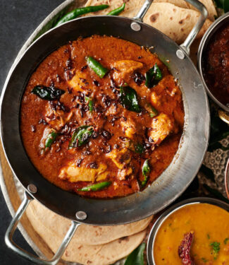 Bowl full of Kerala chicken curry garnished with fried shallots, mustard seed and fried curry leaves - from above.