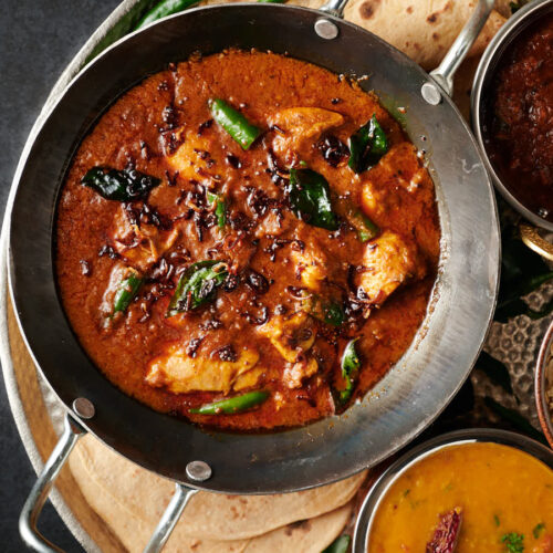 Bowl full of Kerala chicken curry garnished with fried shallots, mustard seed and fried curry leaves - from above.