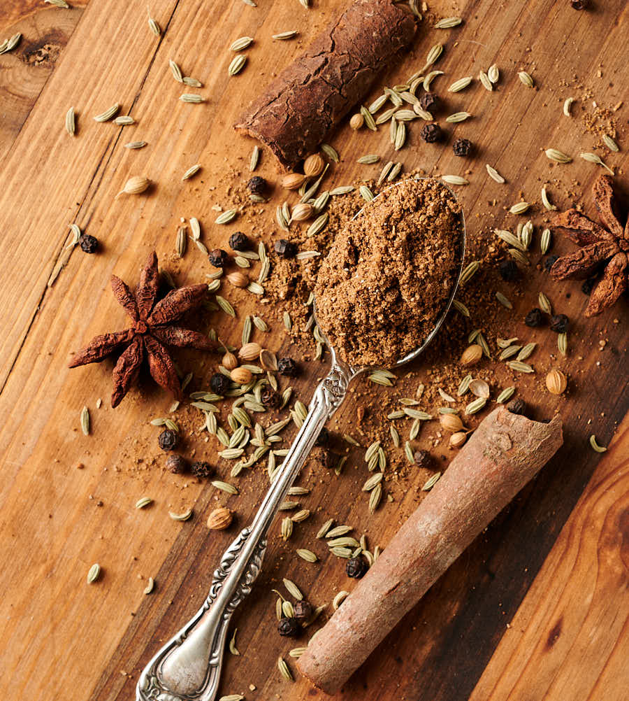 Kerala masala on a spoon surrounded by whole spices from above.