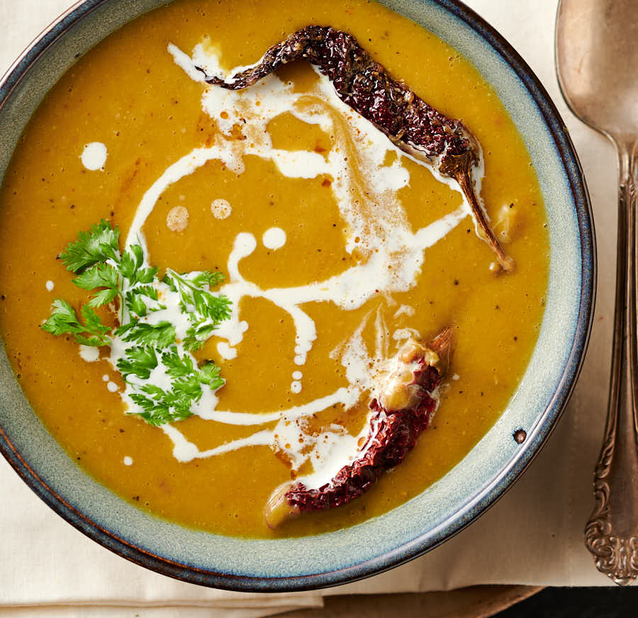 Bowl of mulligatawny soup garnished with kashmiri chilies, cream and cilantro from above.