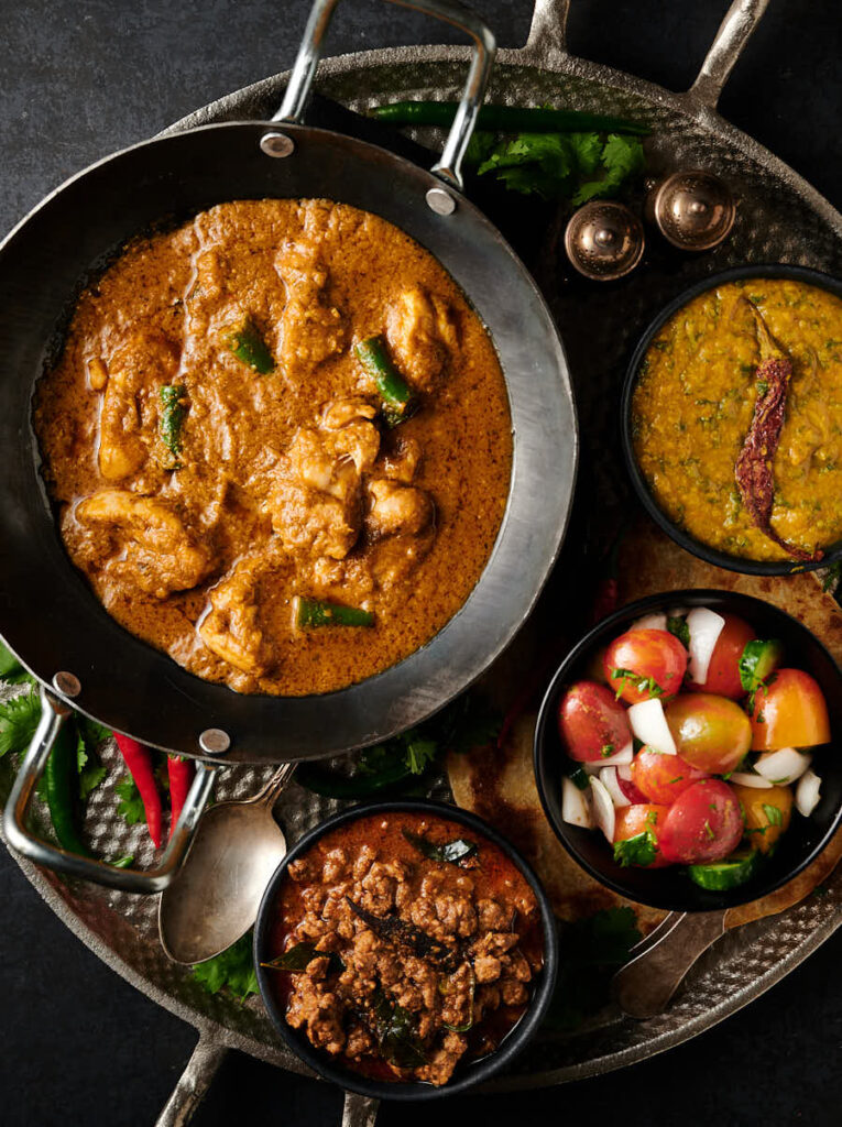 Hariyali chicken curry table scene with bowls of dal, nadan keema and kachumber.