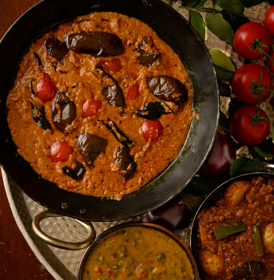 Bagari baingan in a kadai with aloo keema and dal palak from above.