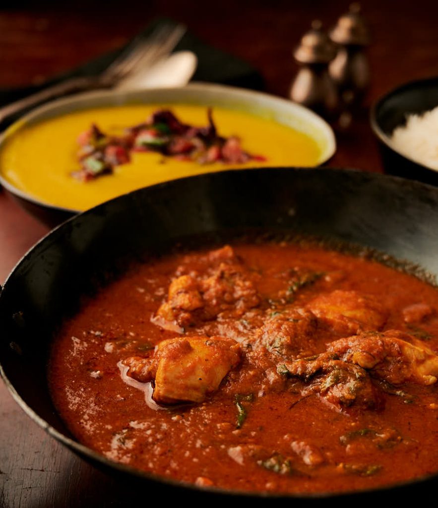 Methi chicken curry in a kadai with dal tarka in the background - from the front