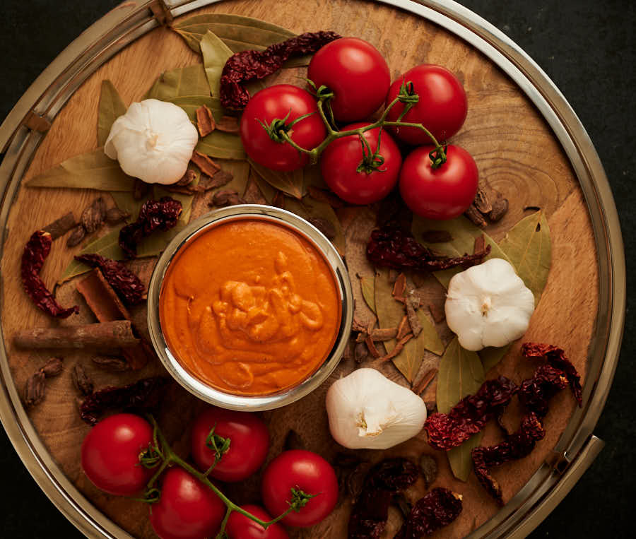 Makhani gravy in a bowl surrounded by fresh tomatoes on the vine.