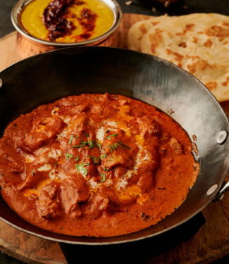 Hotel style butter chicken with parotha in a kadai from the front.