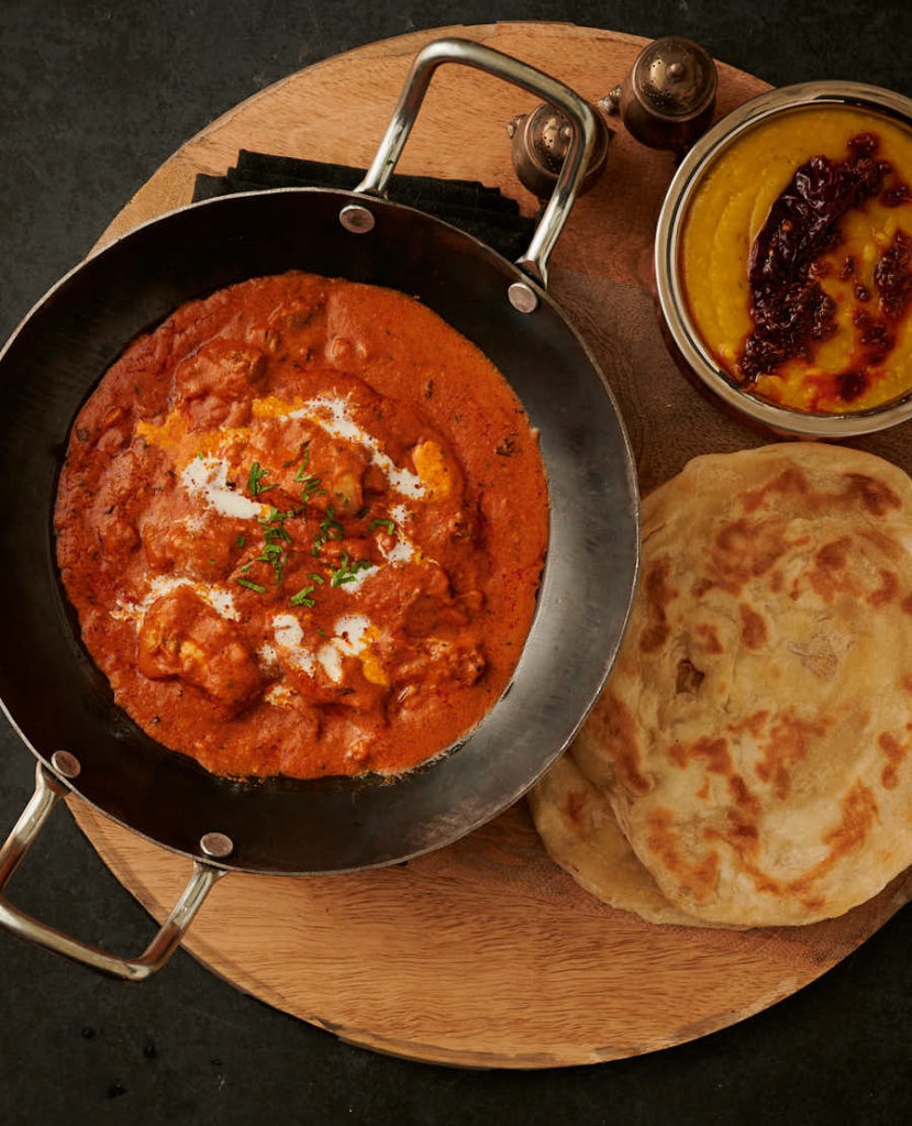 Butter chicken in a kadai table scene with paratha and tarka dal from above.